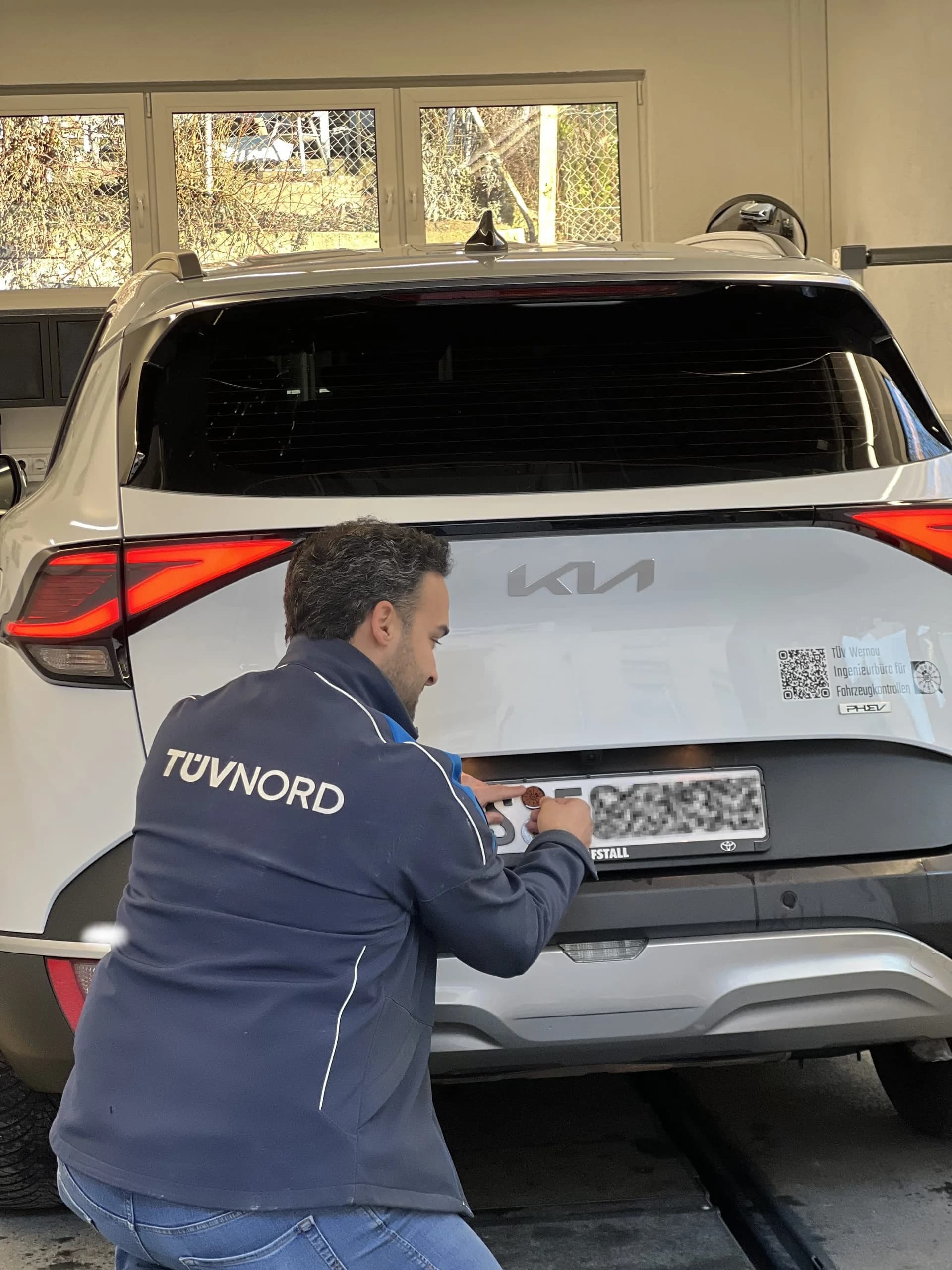 TÜV-Prüfingenieur befestigt die TÜV-Plakette am Kennzeichen